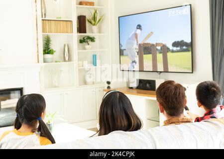 Rear view of family sitting at home together watching cricket match on tv. sports, competition, entertainment and technology concept digital composite Stock Photo