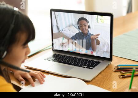 Asian girl using laptop for video call, with smiling elementary school pupil on screen. communication technology and online education, digital composi Stock Photo