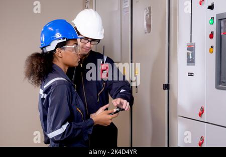 Electrical young woman and man engineer examining maintenance cabinet system electric in the control room at industrial factory, technician or electri Stock Photo