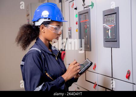 Electrical young asian woman engineer examining maintenance cabinet system electric and using tablet in control room at industrial factory, technician Stock Photo