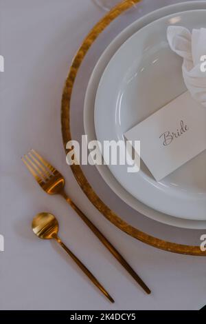 A golden spoon and fork next to a card for the bride lying on a plate on a set wedding table Stock Photo