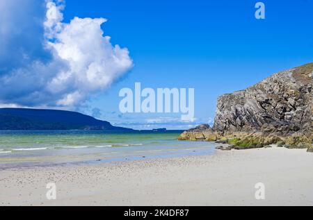 Large white cloud over shadowed Cape Wrath peninsula, Balnakeil Bay and rocky cliff outcrop on white sand beach in sunshine in foreground, Sutherland Stock Photo