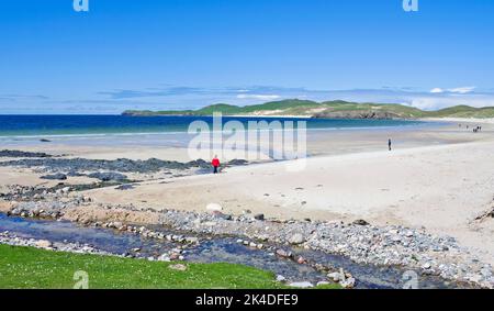 People walking on the white sand beach at Balnakeil Bay, Durness, Sutherland, with the grassy headland of Faraid Head at the far end of the beach. Stock Photo