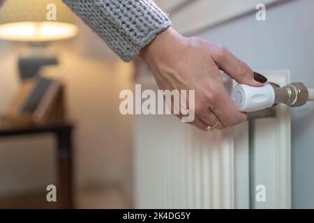 Woman adjusting temperature on heating radiator, Energy crisis concept in Europe, Rising costs in private households for gas bill due to inflation and Stock Photo