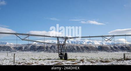 Sprinkler irrigation system on a snow-covered farmland with Ben Ohau range in background, Twizel, South Island. Stock Photo