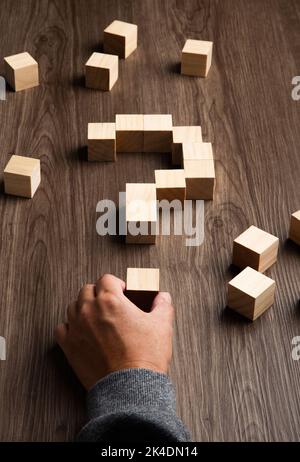 Hand solving a problem, arranging wooden blocks into a question mark on a wooden table Stock Photo