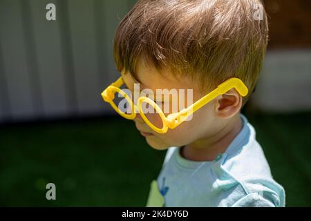 Caucasian blond little boy playing and having fun with a yellow plastic glasses in the schoolyard Stock Photo