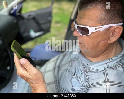 Nice portrait of ukrainian senior in driver seat reading news from cellular screen  in summer time Stock Photo