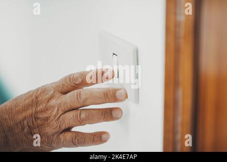 Close up of old hand senior woman switching off or on home light. Concept of saving bills for energy and electricity. Supply reduction in winter. Envi Stock Photo