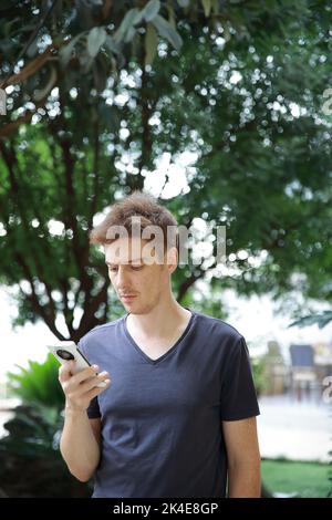 Red haired european man with freckles looking at playing with his mobile phone Stock Photo