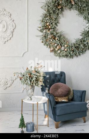 Classic Christmas living room interior. A blue armchair with pillows, a wreath on the wall, and a Christmas tree composition in a vase Stock Photo