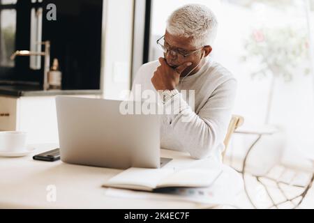 Experienced businessman writing his plans in a notebook while sitting in his home office. Mature businessman using a laptop while working from home. Stock Photo