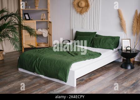 White green bedroom in boho style. A bed, a shelf with decor, a bedside table and a vase with pampas dry grass Stock Photo