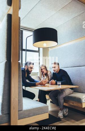 Group of businesspeople working in a co-working space. Three business colleagues using a smartphone during a discussion. Team of diverse entrepreneurs Stock Photo