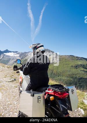 An adventure motorcycle rider at a mountain pass in the Swiss alps. Stock Photo