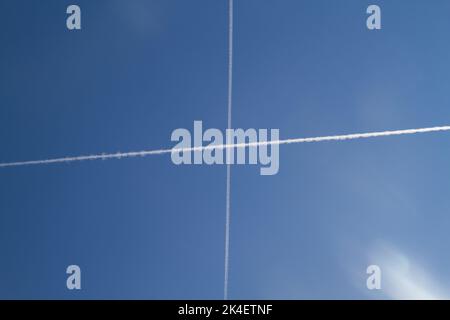 Two condensation trails, contrails or vapor trails in a blue sky, forming a cross in the sky Stock Photo