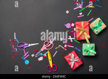 Scissors with gift boxes and confetti on black background Stock Photo
