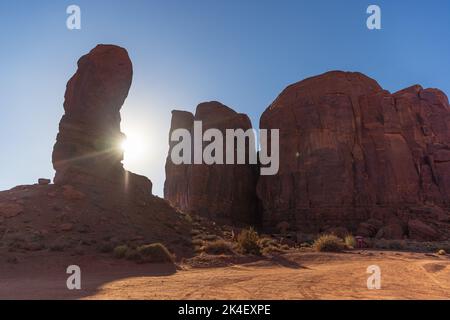Sun setting behind the thumb rock formation at Monument Valley Stock Photo