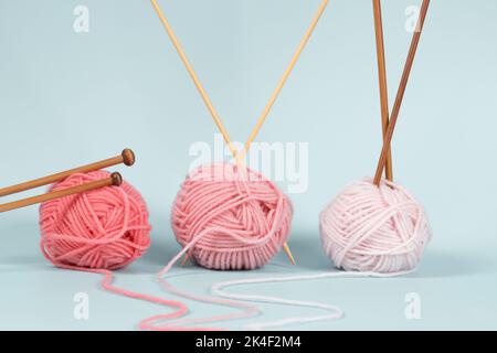 Three yarn balls with wooden bamboo knitting needles on light blue background. Hobby, relaxation, mental health, sustainable lifestyle Stock Photo