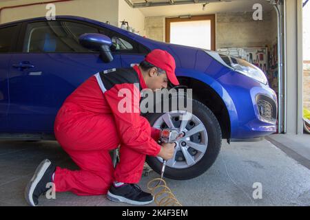 Picture of a mechanic in his workshop who with a pneumatic screwdriver disassembles the wheel of a car resting on trestles. Car repair work Stock Photo