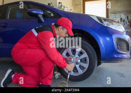 Tire dealer who disassembles the wheels of a tire changing machine with a pneumatic screwdriver. Tire replacement for season change Stock Photo
