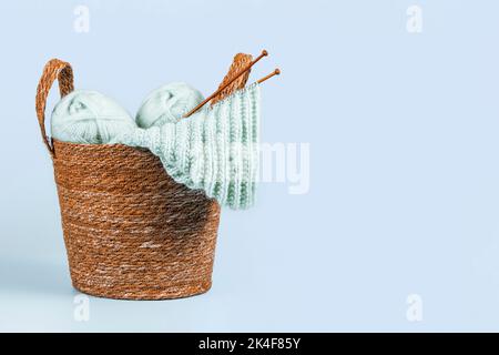 Knitting background. Knitting yarn, bamboo needles and new started knitted sweater in basket on light blue background. Handmade hobby, relaxation at Stock Photo