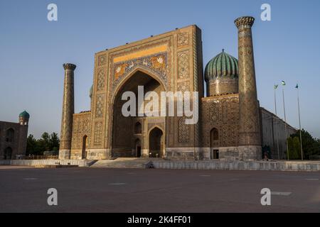 Sherdor Madrassa in the Registan complex featuring intricate blue tile arch with sunrays hitting the tops at sunset, Samarkand Stock Photo