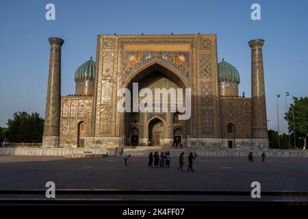Sherdor Madrassa in the Registan complex featuring intricate blue tile arch with sunrays hitting the tops at sunset, Samarkand Stock Photo