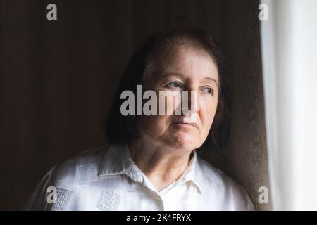 Elderly woman standing and looking through the window. Stock Photo