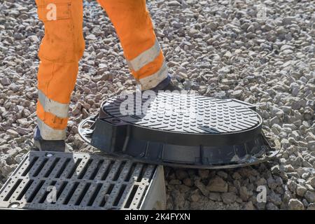 Installing cast iron sewer hatch on a concrete base of installation of water sewer well in the ground at construction site Stock Photo