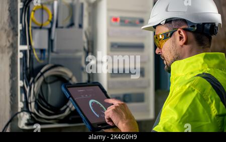 Man an electrical technician working in a switchboard with fuses, uses a tablet. Stock Photo