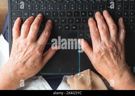 Elderly woman hands typing on the laptop keyboard. Top view Stock Photo