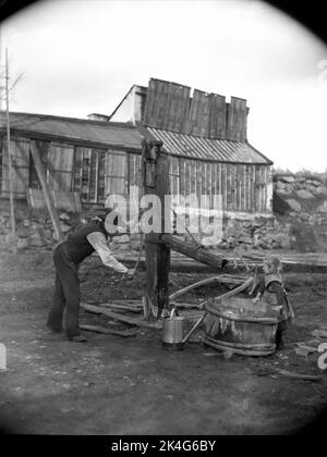 A man pumping water and a little girl at an old pump. Variant of the photo 'The Old Pump' (Stockholm City Museum). There with two women and one boy. About 1880-1890. Eriksberg area, Ladugårdsland parish, Stockholm. In the background a greenhouse. Nordic Stock Photo