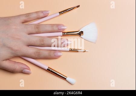 Many different make up brushes in woman hand close up view on beige color background Stock Photo