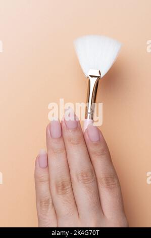 Hand hold cosmetic brush close up view on beige color background Stock Photo