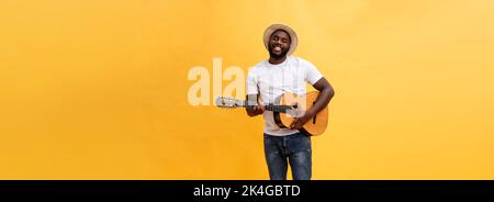 Full-length photo of excited artistic man playing his guitar. Isolated on yellow background. Stock Photo