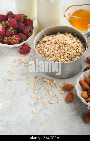 Ingredients for cooking oatmeal or granola with oats, milk, raspberries, honey and almonds on gray concrete old table background. Ingredients for heal Stock Photo