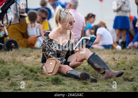 Green Man Festival 2019 – a popular music festival in Wales, UK. Photo credit: Rob Watkins. Pictured: A woman in muddy boots reading Caitlin Moran Stock Photo