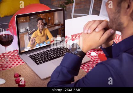Diverse couple making valentines date video call the woman on laptop screen laughing. online valentines day during quarantine lockdown. Stock Photo