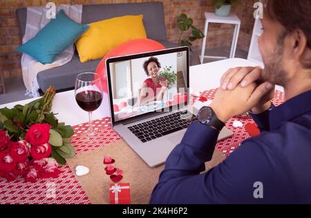 Diverse couple making valentines date video call the woman on laptop screen smiling. online valentines day during quarantine lockdown. Stock Photo