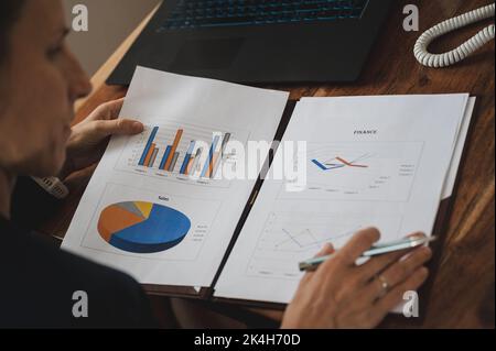 Over the shoulder view of young businesswoman reading and reviewing business statistical data sales report in a folder. Stock Photo