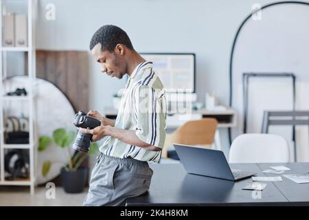 Minimal side view portrait of black photographer holding camera and looking at images in studio setting, copy space Stock Photo