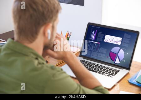 Caucasian businessman sitting at desk using laptop with graph and statistical data on screen. business communication and digital interface technology Stock Photo