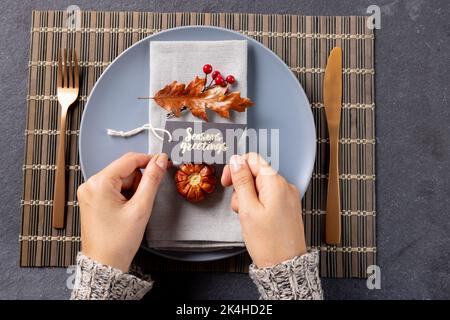 Overhead view of thanksgiving place setting with caucasian woman holding greetings tag on slate Stock Photo