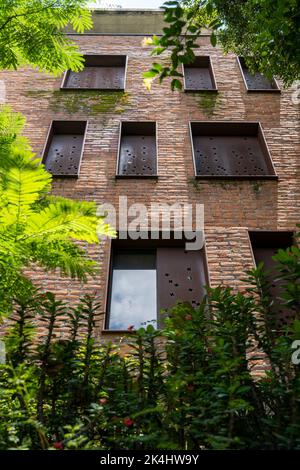 building windows surrounded by plants vegetation, corten steel windows, rusted steel, red brick building, crosses perforated in steel Stock Photo