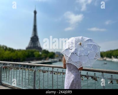 the perfect backdrop for any story about Paris a slender girl looks up at the Eiffel Tower but all we see is a parasol and a blue sky the photo is calm and interesting like a picture. High quality Stock Photo