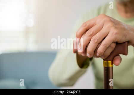 Closeup hands of senior disabled man holding walking stick, Old man sitting resting on sofa hold wooden walking cane, Elderly hand holding handle of c Stock Photo