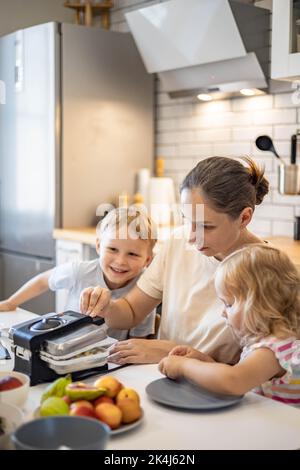 Happy family cooking baking waffles together enjoying weekend breakfast at kitchen home Stock Photo