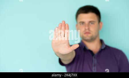 Stop gesture. Confident man. Closed way. Serious defocused guy in t-shirt holding forbidden hand up expressing protest isolated blue copy space. Stock Photo