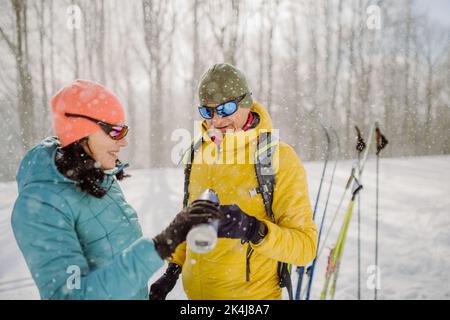 Senior couple resting and drinking hot tea from thermos in the middle of snowy nature. Stock Photo